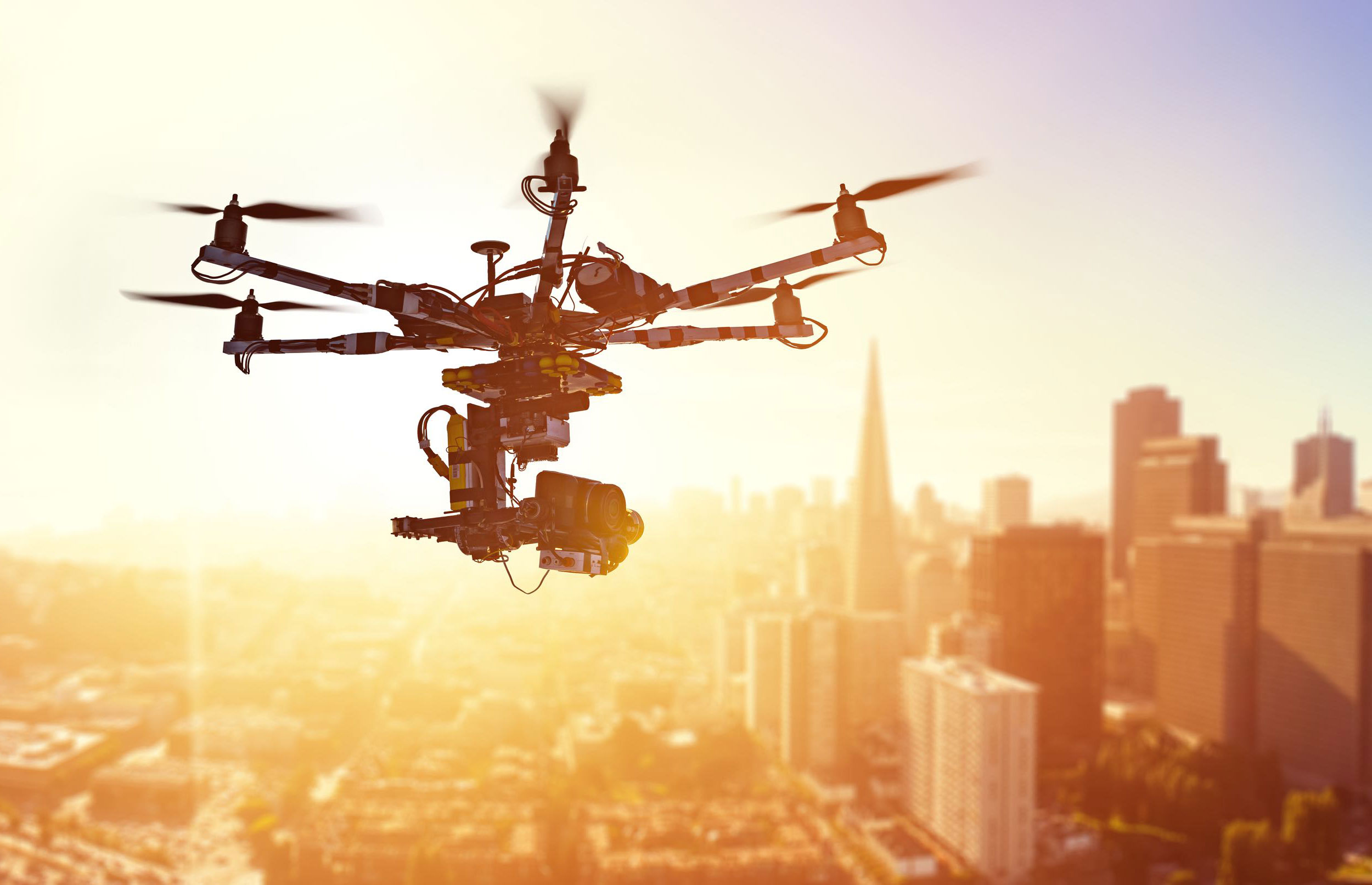 drone flying in the air with sunset and city behind the drone